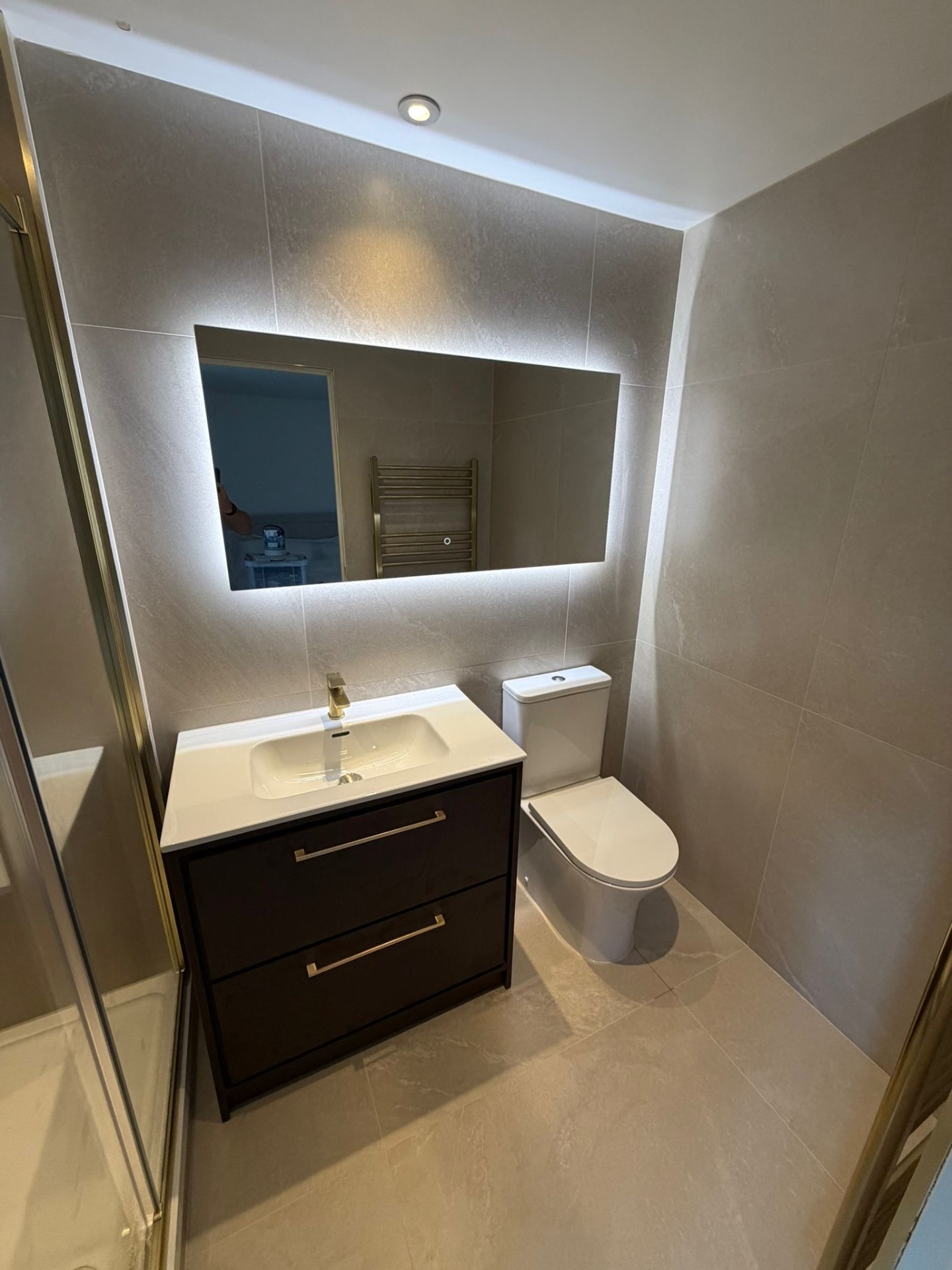 Modern ensuite with illuminated mirror, dark vanity and neutral stone tiles