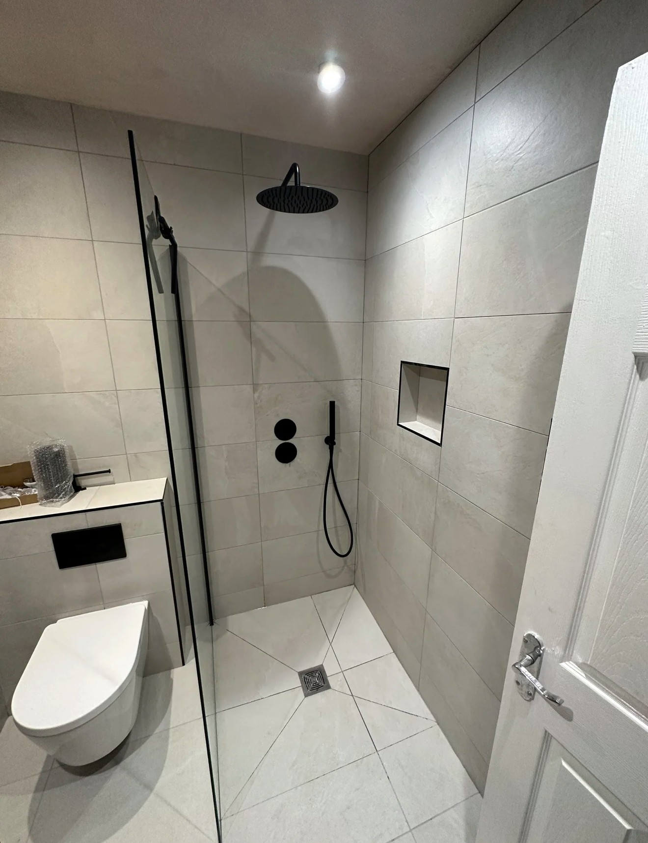 Compact grey wet room with matte-black rainfall shower and wall-hung toilet