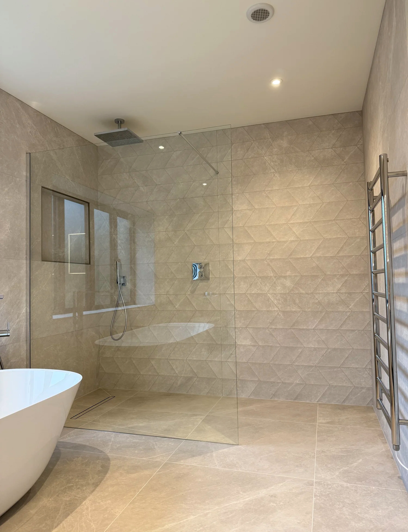 Luxury beige-tiled wet room with frameless glass shower and freestanding bath